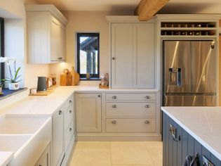 A shaker kitchen with light grey cabinets, a large stainless steel fridge, and wooden cutting boards. A window with a potted orchid adds natural light.