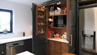 Shaker kitchen with an open pantry cabinet revealing spices, a microwave, and small appliances. A sleek fridge with a water dispenser is on the right.