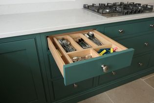 Open kitchen drawer with utensils neatly organized in wooden dividers. The drawer is in a green cabinet beneath a white countertop and gas stove.