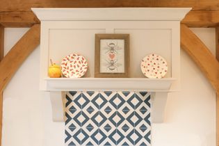 A white shelf holds a bee-themed framed picture and two decorative plates with red and orange motifs. Below, blue diamond-patterned tiles add contrast.