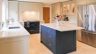 Elegant kitchen with cream cabinetry, a dark blue island with vase and flowers, stainless steel fridge, black oven, and beige tiled floor.