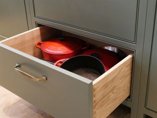 A kitchen drawer with a green exterior and wooden interior contains neatly arranged cookware, including a red Dutch oven and pots, conveying organization.