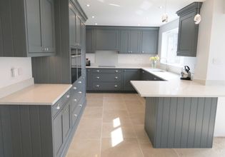 Shaker kitchen with sleek grey cabinets, quartz worktop, and beige tiled floor. Pendant lights hang above creating a clean, elegant ambiance.