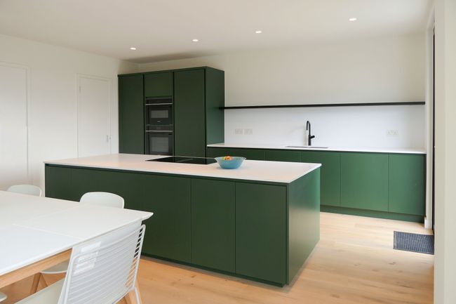 Modern kitchen with sleek green cabinets and white countertops. Central island and integrated appliances create a minimalist, spacious feel.