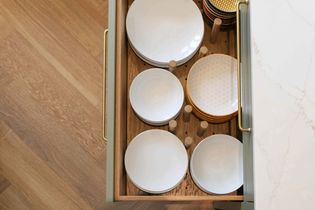 Open drawer with neatly stacked white and patterned plates and bowls, organized with wooden pegs. The setting conveys a sense of order and elegance.