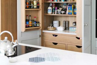 Kitchen scene with open pantry filled with spices, cans, and jars. A white countertop holds a silver kettle and kitchen items