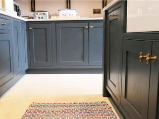 A cozy shaker kitchen with elegant dark grey cabinets and gold handles. A colourful woven rug on the floor adds a touch of warmth, complemented by a bread box and toaster on the countertop.