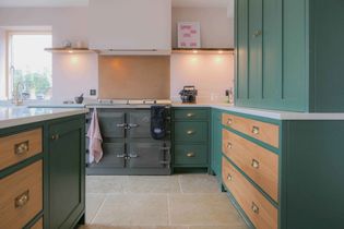 A shaker kitchen with green cabinets and natural wood drawers. An electric stove is in the center, under a hood. Warm lighting creates a welcoming ambiance.