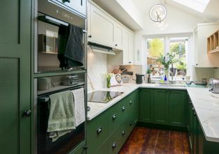 Dark green shaker cabinetry with cream cabinets above, a double oven in the front with a kitchen sink, kettle and radio in the background