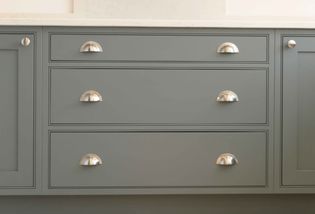 Grey kitchen cabinet drawers with sleek, metallic cup handles. The surface is clean and modern, conveying a minimalist and contemporary vibe.