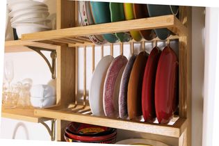 Wooden kitchen shelves with neatly stacked colorful plates and bowls. Glassware and white dishes are also stored, conveying an organized and tidy space.