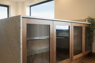 A minimalist kitchen with a speckled countertop and wooden cabinets featuring glass doors. Greenery adds a natural touch. Bright and modern.
