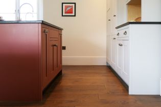 Shaker kitchen with a reddish-brown island, white cabinets, dark countertops, wood flooring, and a framed fish illustration.