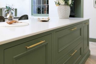 A stylish kitchen island with sage green cabinets and gold handles sits beneath a quartz countertop. A vase with flowers and decor accents add elegance.