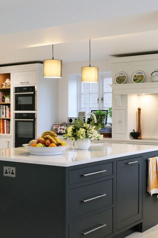 Shaker kitchen with a large island featuring dark cabinets and surrounding perimeter in white with a bright countertop. A bowl of fruit and a vase of white flowers add a fresh touch.