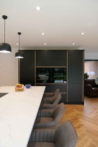 Modern kitchen with black cabinetry, marble countertop island, four grey chairs, wooden floor, and pendant lights above.