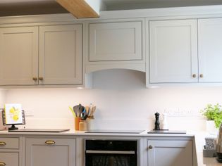 Shaker kitchen with light grey cabinets, sleek white countertops, and under-cabinet lighting. Accessories include utensils, a cookbook, and a potted herb.