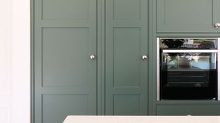 Close up of sleek green shaker kitchen cabinetry with silver knobs, featuring a built-in modern oven.
