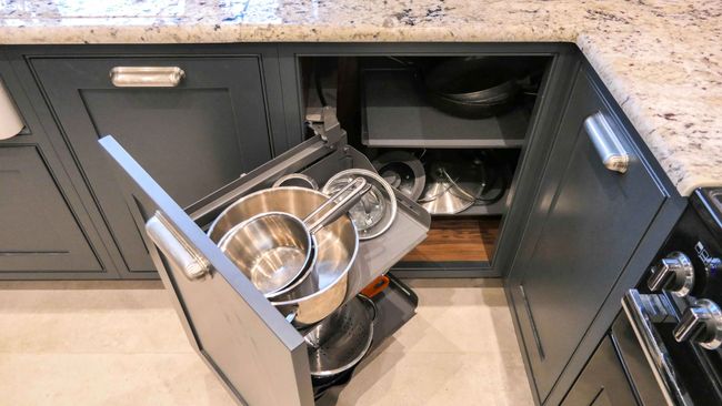 Shaker kitchen with dark grey cabinetry featuring a pull-out drawer filled with stainless steel bowls and pots, conveying a tidy and efficient storage solution.