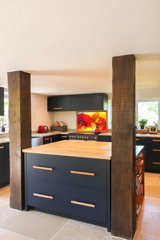 modern kitchen with navy blue cabinets, central island with wooden beams either side and hardwood oak worktop. Yellow and red abstract splashback in the background