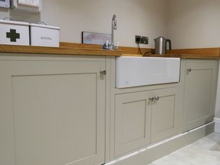 A utility room features cream cabinets with silver knobs, a farmhouse sink, and wood countertops. Items include a kettle and storage tins.