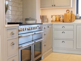 Shaker kitchen with a stainless steel oven and splashback. Light grey cabinets, wooden cutting boards, and glass jars on the counter. Bright and inviting.