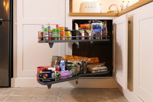 Shaker kitchen cabinet with a corner pull-out shelf, displaying various packaged groceries like jars, cans, and snacks in an organised manner.
