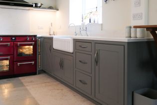 A shaker kitchen with a red range, grey cabinets, and a white farmhouse sink. The countertop holds ceramic jars, creating a cozy atmosphere.