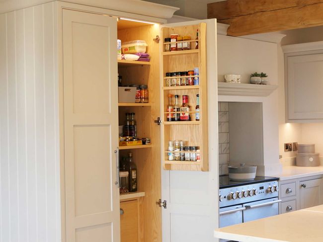 A well-organised kitchen pantry with an open door reveals neatly arranged spices and jars on the shelves. The kitchen features a range and neutral tones.