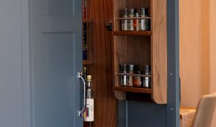 Open navy blue kitchen cabinet revealing spice shelves and bottles inside. Warm, inviting kitchen ambiance with a focus on organisation and storage.