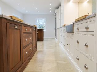 Spacious shaker kitchen with a polished floor. Features contrasting wooden and white cabinets, silver handles, warm lighting, and a large window.