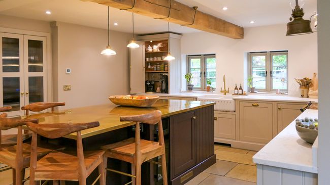 Warm, spacious Shaker kitchen with cream cabinets, a large dark island, rustic stools, exposed beams, and pendant lighting.