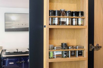 Oak spice rack built into a cupboard door, holding jars and tins, in a navy kitchen