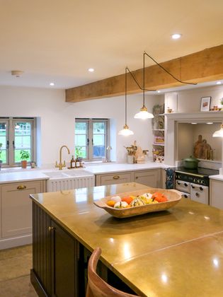 Warm country-style Shaker kitchen with a central island, pendant lights, windows, and a bowl of colourful vegetables.