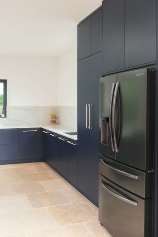 Modern kitchen with dark blue cabinets and a sleek black refrigerator on the right. Light beige floor tiles and marble effect backsplash add elegance.