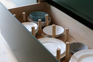 An open drawer with wooden dividers neatly organizing white and blue plates on a light wood base, conveying a sense of order and cleanliness.