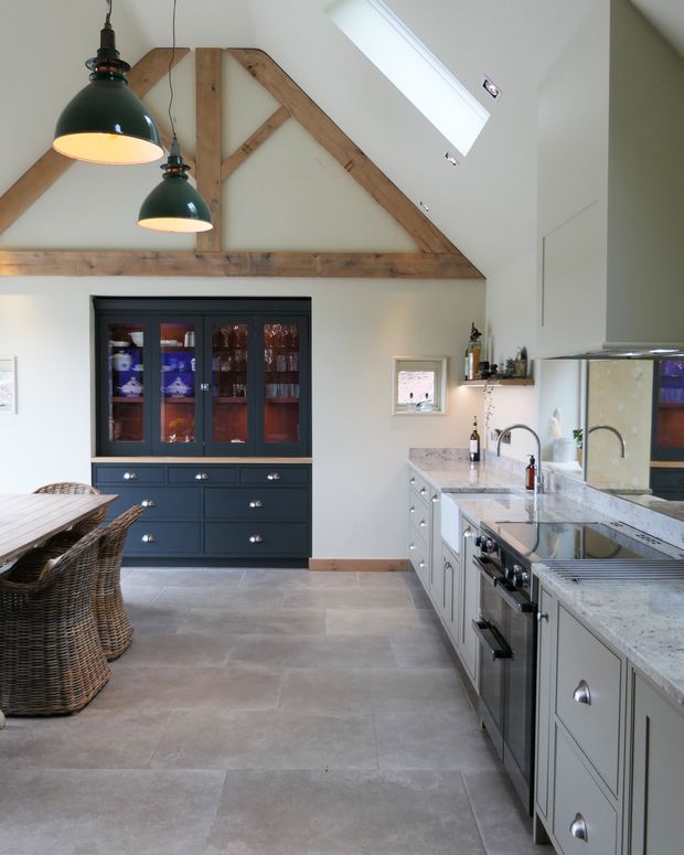 Shaker kitchen with exposed wooden beams, green pendant lights, glass-front dish cabinets, and a large stone-topped island.