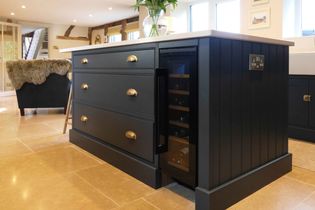  Shaker kitchen with a dark island featuring brass handles and a built-in wine fridge.