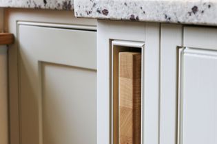 Close-up of a pale kitchen cabinet with a speckled worktop. A wooden cutting board is partially visible in a built-in side slot.