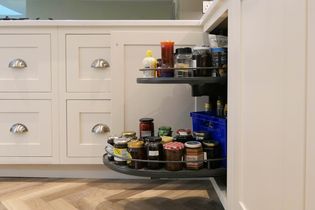 A kitchen cabinet with a pull-out shelf displays various jars and bottles of condiments and spices, adding organization and accessibility.