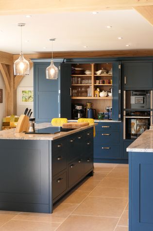 Shakerkitchen with navy blue cabinets, open shelving displaying dishes, and marble countertops. A cozy atmosphere with pendant lighting and wood beams.