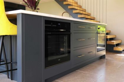 Bespoke dark navy kitchen island with integrated ovens and brass bar handles, made to fit the space