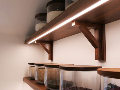 Slimline LED strip lighting under an walnut shelf with glass storage jars