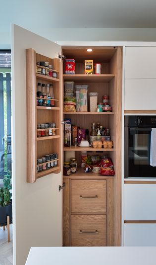 A modern kitchen pantry with organised shelves, containing various spices, jars, and containers, alongside a range of snacks and food items.