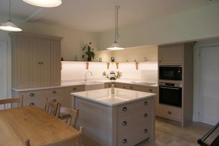 A shaker kitchen with beige cabinets, a center island, and wooden chairs. Soft lighting and plants create a cozy, inviting atmosphere.