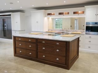 Luxurious shaker kitchen with a large walnut wooden island, light worktop, modern white cabinets, built-in oven, and ceiling spotlights. Bright and elegant ambiance.