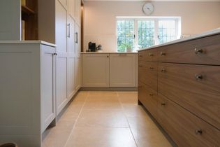 Modern kitchen with cream cabinets, a wooden island, and beige floor tiles. Sunlight streams through a window above the sink. Calm and inviting.