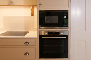 Shaker kitchen with beige cabinetry, featuring a built-in oven and microwave. A stovetop is integrated into the countertop. Warm, inviting ambiance.