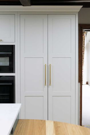 Neutral kitchen cabinets with tall gold handles and integrated appliances. A wooden counter in the foreground adds warmth. Calm, modern ambiance.