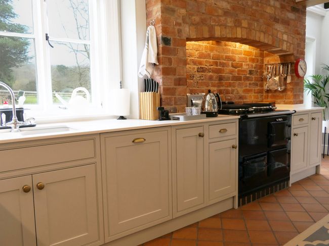 Shaker kitchen with light grey cabinets, displaying the brick fireplace and oven sat within it.